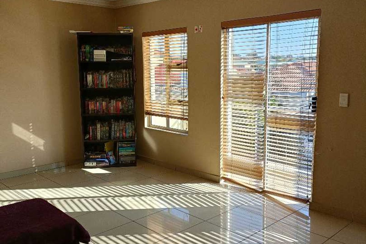 A bright living room featuring large tiled floors, natural light through sliding glass doors, and venetian blinds, offering a clean and functional living space.