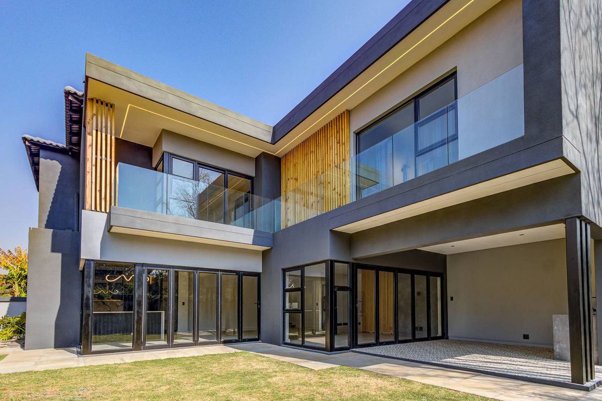 Modern double-storey cluster home featuring contemporary dark facade, glass balustrades, extensive stacking doors, and timber slat accents overlooking a private garden.