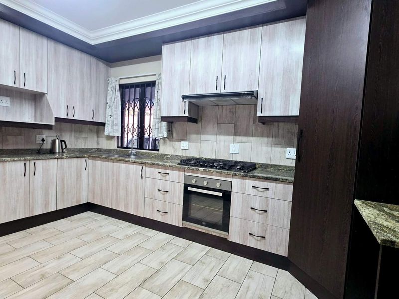 A well-maintained kitchen featuring light wood-grain cabinetry, granite countertops, built-in oven, gas hob, and tiled flooring.