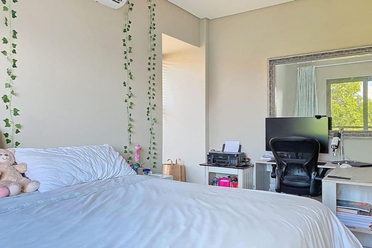 A well-lit bedroom featuring neutral wall tones, an integrated air conditioning unit, and a window providing natural light.