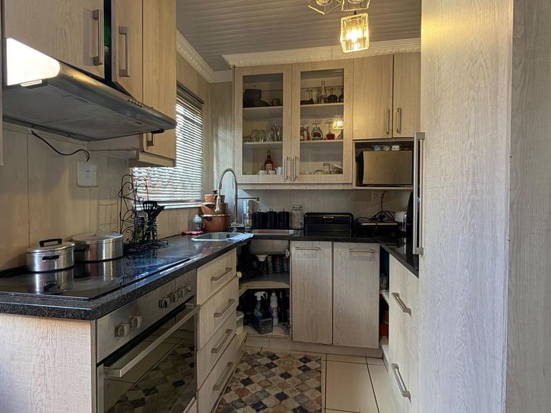 Compact kitchen featuring light wood-grain cabinetry, dark laminate countertops, built-in oven with hob, and an extractor fan.