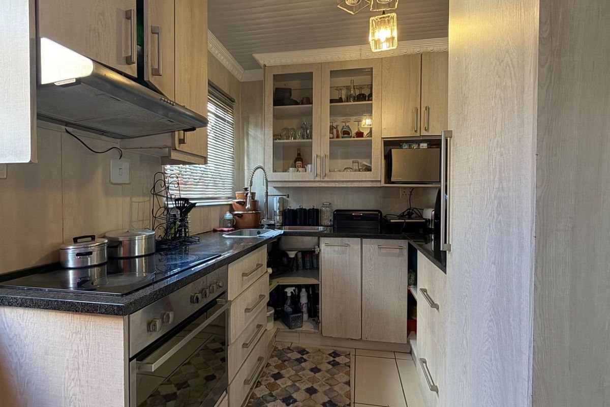 Compact kitchen featuring light wood-grain cabinetry, dark laminate countertops, built-in oven with hob, and an extractor fan.