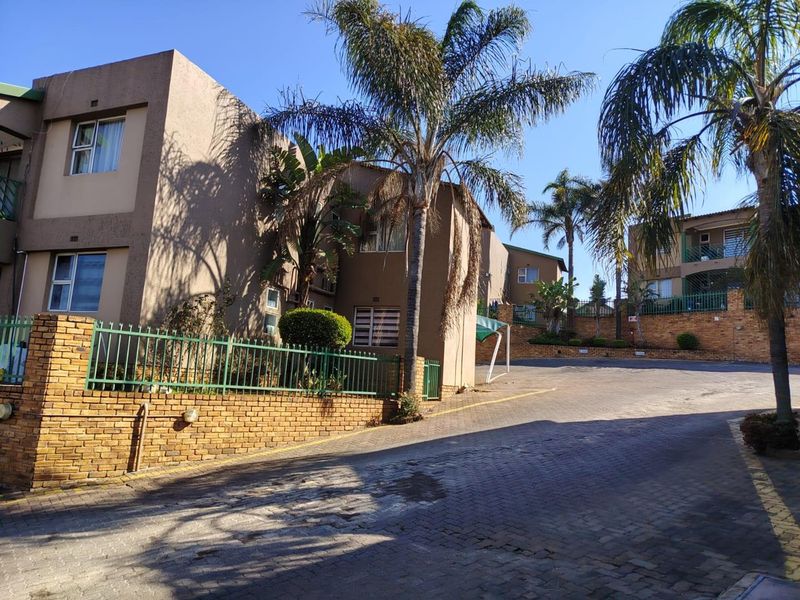 Exterior view of a multi-story townhouse complex featuring a paved driveway, brick boundary walls, and established landscaping.