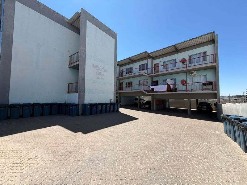 Exterior view of the Willoreid Close apartment complex featuring paved parking, external staircases, and multi-level residential units with metal balcony railings.