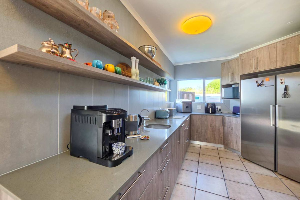 Modern kitchen featuring stone countertops, wood-finish cabinetry, floating shelving, and tiled flooring, offering a clean and functional workspace.