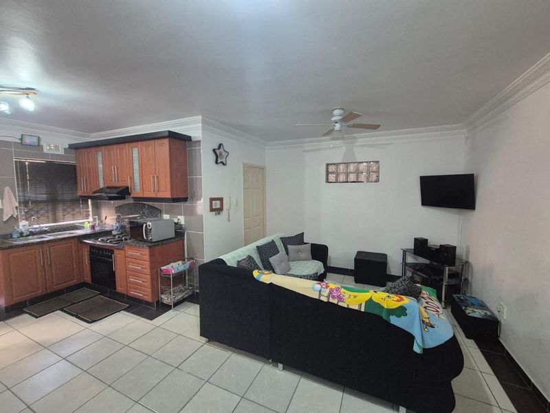 Open-plan living area featuring a functional kitchen with built-in cabinetry, hob, oven, and extractor fan, seamlessly flowing into the lounge space with tiled flooring.