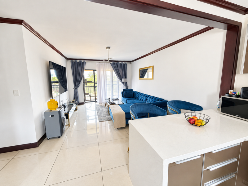 Spacious open-plan living area featuring polished porcelain tiles, crown molding, and a modern kitchen island with quartz countertops, leading to a private balcony.