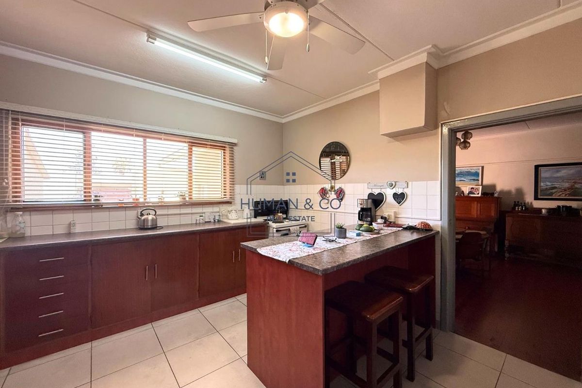 A functional kitchen featuring wooden cabinetry, a breakfast bar, tiled flooring, and a ceiling fan, offering a practical layout for daily meal preparation.