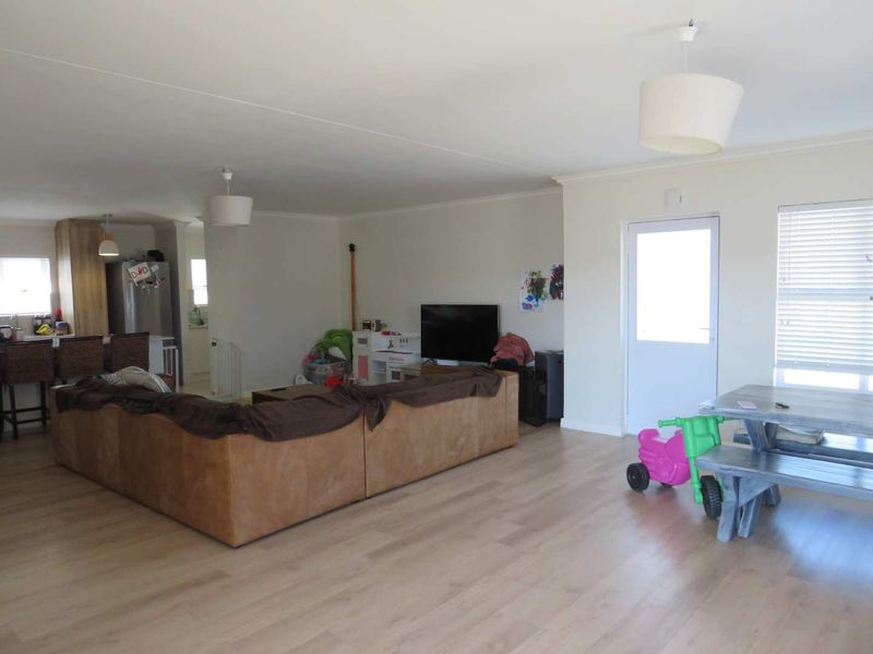 Spacious open-plan living area featuring light laminate flooring, neutral walls, and an integrated kitchen with island, offering a versatile layout for family living.