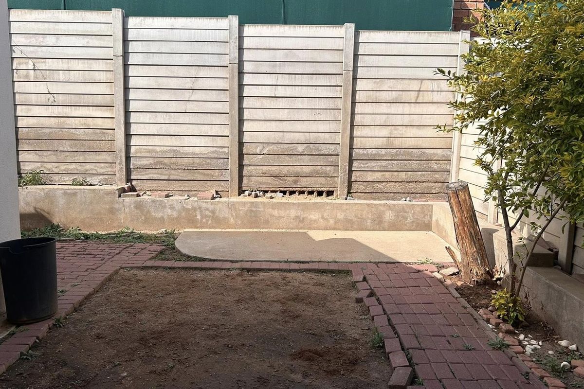 A compact rear courtyard featuring a precast concrete boundary wall, a small concrete retaining wall, and brick-paved pathways.