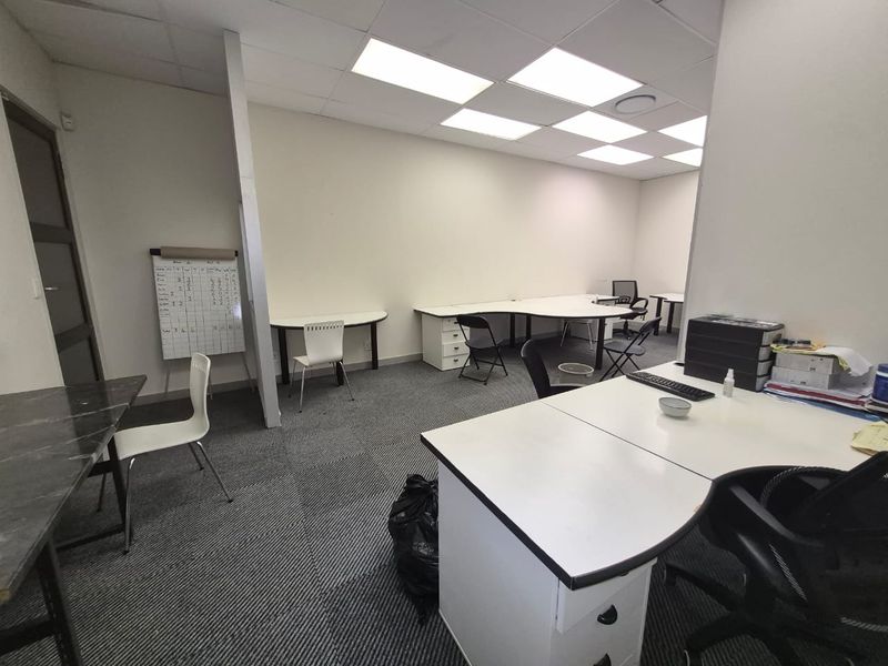 A functional office space featuring a suspended ceiling, recessed lighting, and carpeted flooring, equipped with built-in desk units.