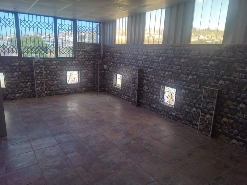 An empty, open-plan living space featuring tiled floors and decorative brick-effect wall cladding with security-barred windows.