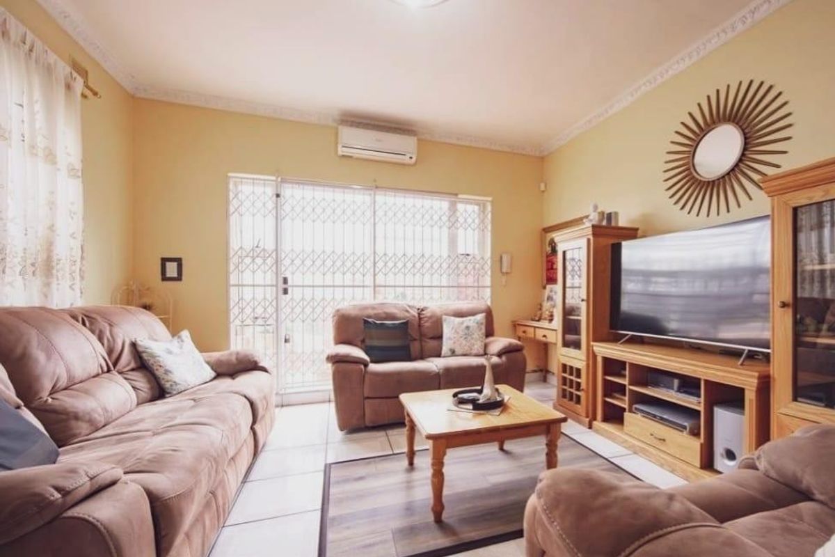 A comfortable living room featuring tiled flooring, decorative ceiling cornices, and a wall-mounted split-system air conditioner with access to an outdoor area via a security gate.