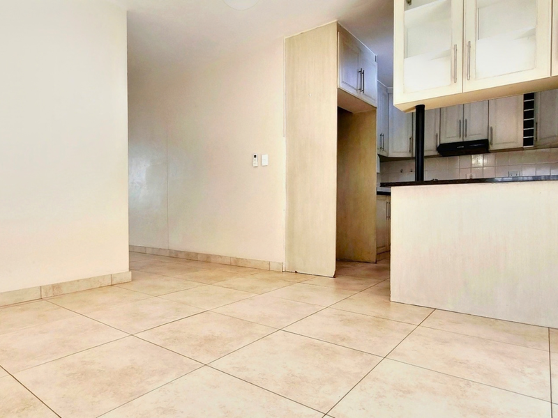 An open-plan living and kitchen area featuring neutral tiled flooring, built-in cabinetry, and a breakfast bar, offering a blank canvas for interior design.