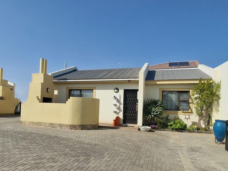 Front elevation of a townhouse featuring a paved driveway, built-in outdoor braai area, and solar water heating system on the roof.