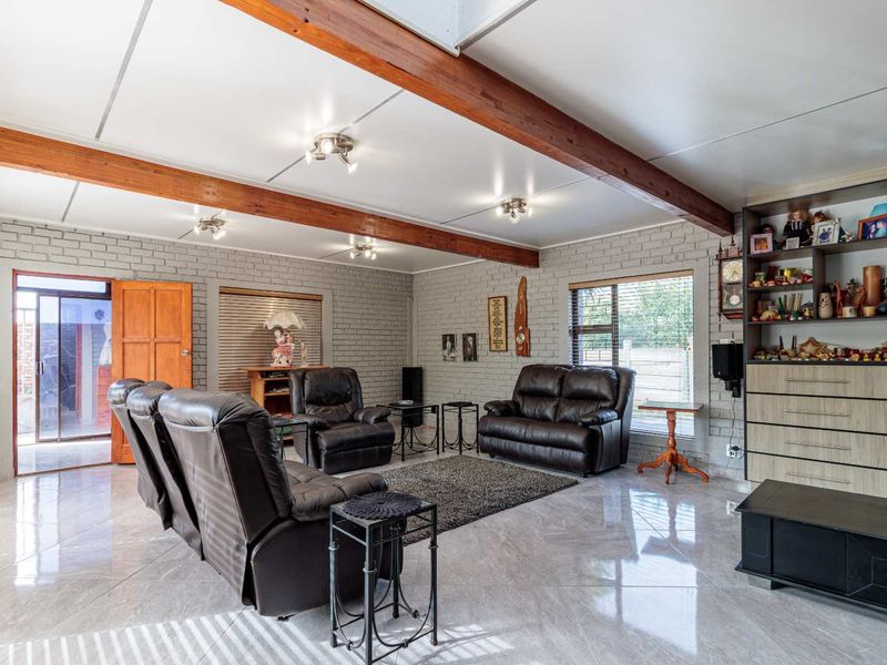 Spacious living room featuring exposed timber ceiling beams, painted brick walls, polished tiled flooring, and a skylight, offering a bright and open living environment.