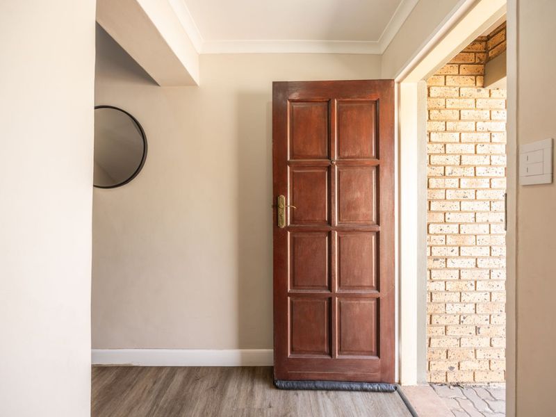 A bright and welcoming entrance area featuring a classic timber panelled front door, neutral walls, and durable laminate flooring.
