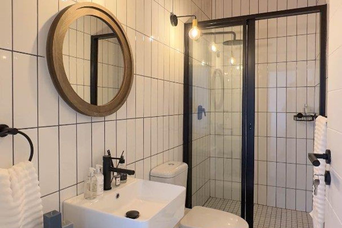 Modern bathroom featuring a walk-in shower with black frame, wall-mounted basin, and distinctive wood-paneled ceiling with subway tile walls.