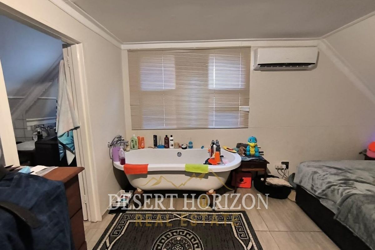 A bedroom featuring a freestanding bathtub, split-system air conditioning unit, and tiled flooring, with an adjoining bathroom visible through the doorway.