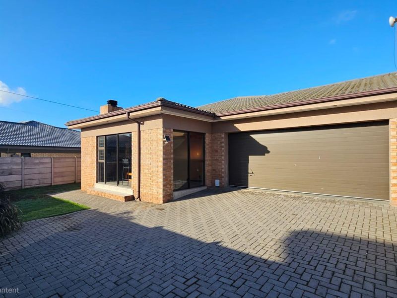 Front exterior view of a brick house featuring a paved driveway, a double garage with a sectional door, and aluminium-framed windows.