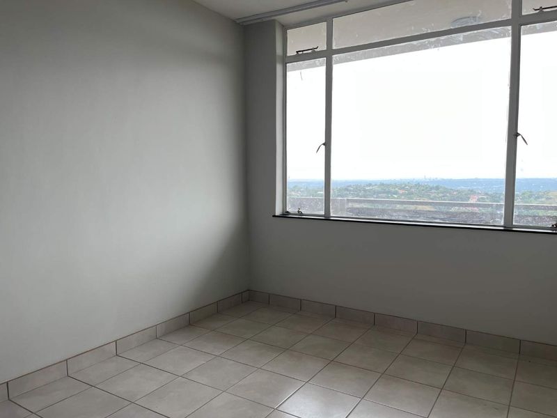 An empty bedroom featuring tiled flooring and a large window with expansive views, providing a blank canvas for personalization.