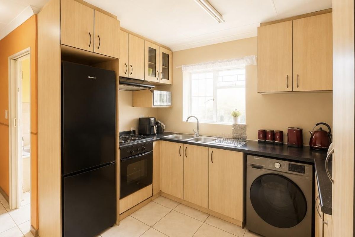 A functional kitchen featuring light wood cabinetry, laminate countertops, a built-in oven with gas hob, and tiled flooring.