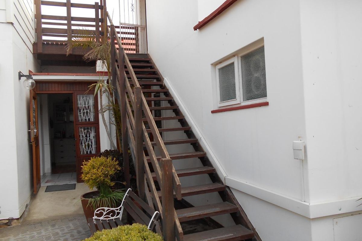 Exterior view of a rear courtyard featuring a timber staircase leading to an upper level, with access to the main dwelling entrance.