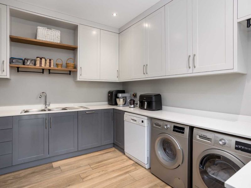 Modern laundry room featuring sleek two-tone cabinetry, quartz countertops, stainless steel sink, and integrated space for laundry appliances.