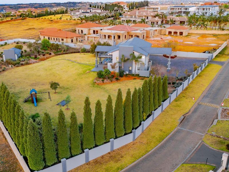 Aerial view of a residential property featuring a large landscaped garden, perimeter wall, and paved driveway within a suburban estate.