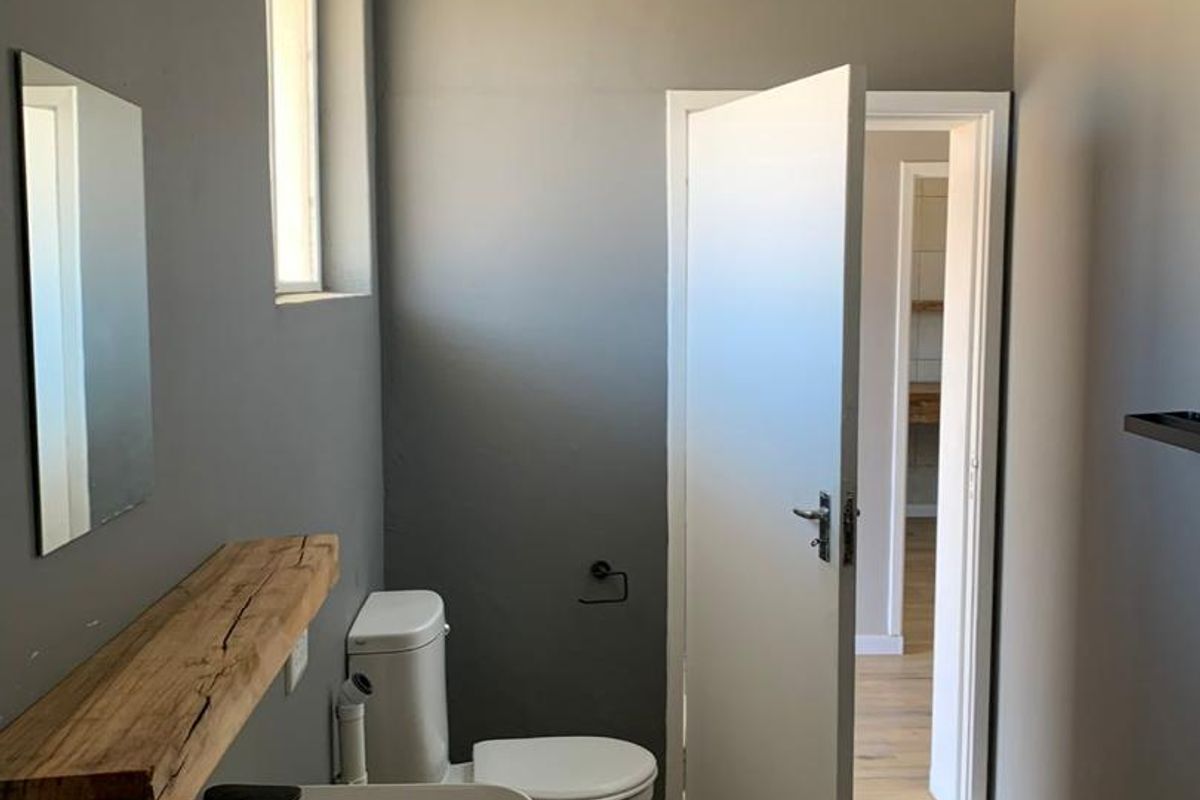Modern bathroom featuring a vessel sink, wooden vanity shelf, wall-mounted mirror, and a white toilet with wood-look flooring.