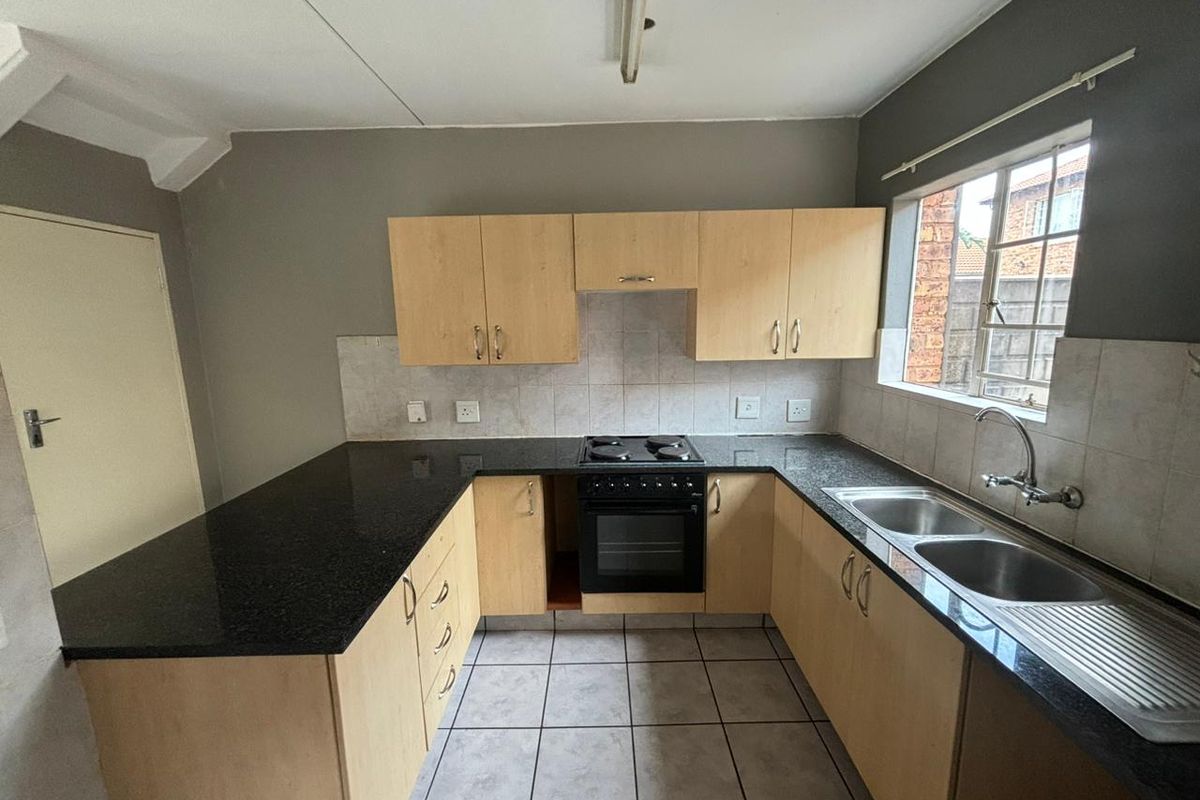 Functional kitchen featuring light wood cabinetry, dark granite countertops, a built-in oven with hob, and a double stainless steel sink.