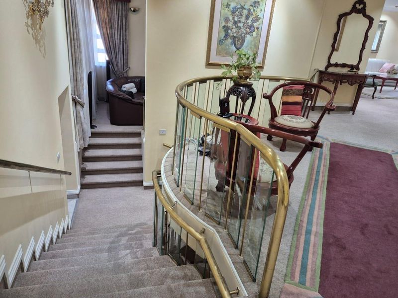 A carpeted staircase featuring a curved glass balustrade with a brass handrail, leading to an upper landing area.