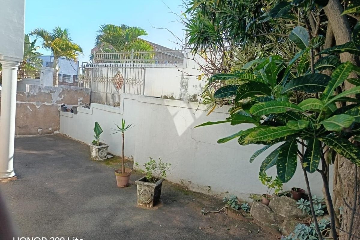 A rear outdoor area featuring concrete paving, a structural column, and a boundary wall with metal security fencing.
