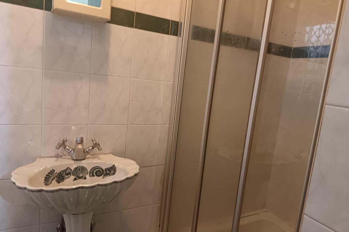 A compact bathroom featuring a pedestal basin and a shower enclosure with tiled walls.
