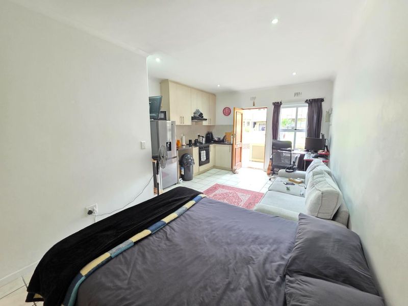 Open-plan studio apartment featuring a compact kitchen with built-in cabinetry, tiled flooring, and direct access to an outdoor area.