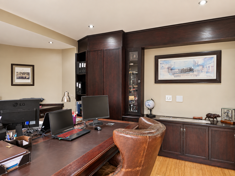 A professional home office featuring custom dark wood built-in cabinetry, recessed lighting, and polished hardwood flooring.