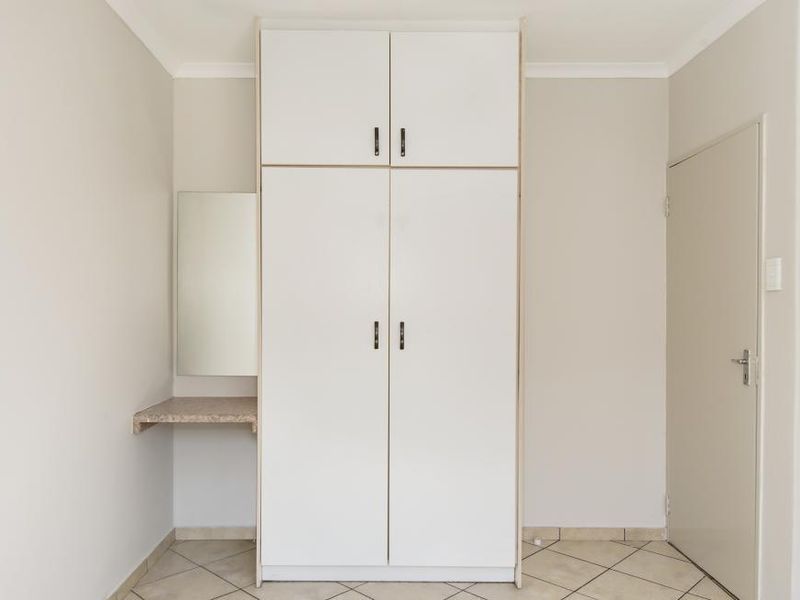 A clean bedroom interior featuring a white built-in wardrobe with overhead storage and an integrated vanity area with tiled flooring.