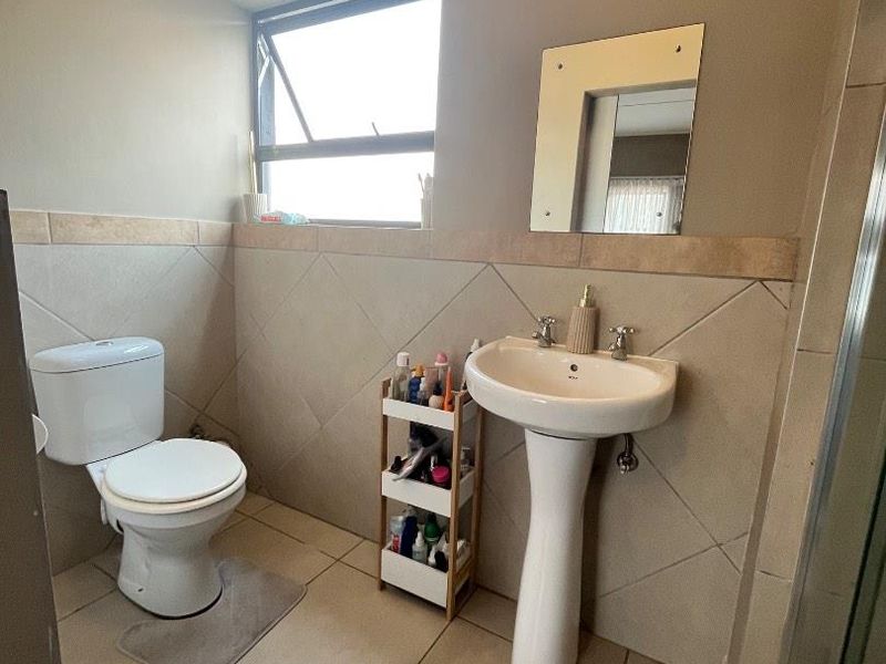 A functional bathroom featuring a pedestal basin, toilet, tiled flooring, and wall tiling with a top-hung window for natural light.