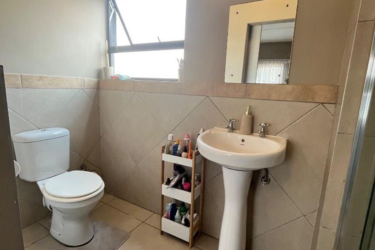 A functional bathroom featuring a pedestal basin, toilet, tiled flooring, and wall tiling with a top-hung window for natural light.