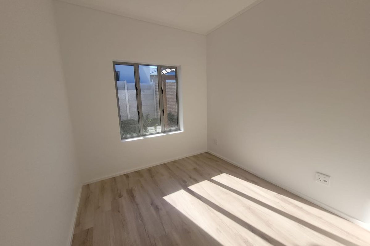 A bright, empty bedroom featuring light-toned wood-look flooring, neutral white walls, and a window providing natural light.