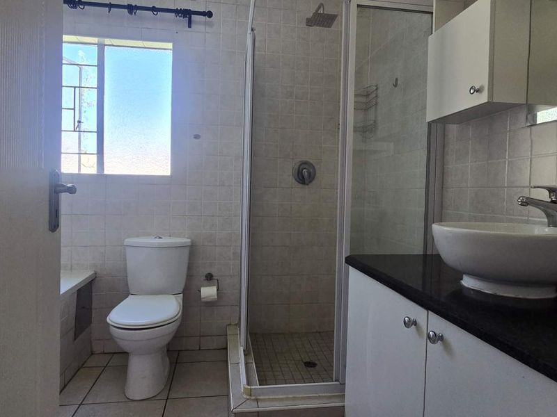 A functional bathroom featuring a shower enclosure, vanity with vessel sink, and tiled finishes, offering a clean and practical layout.