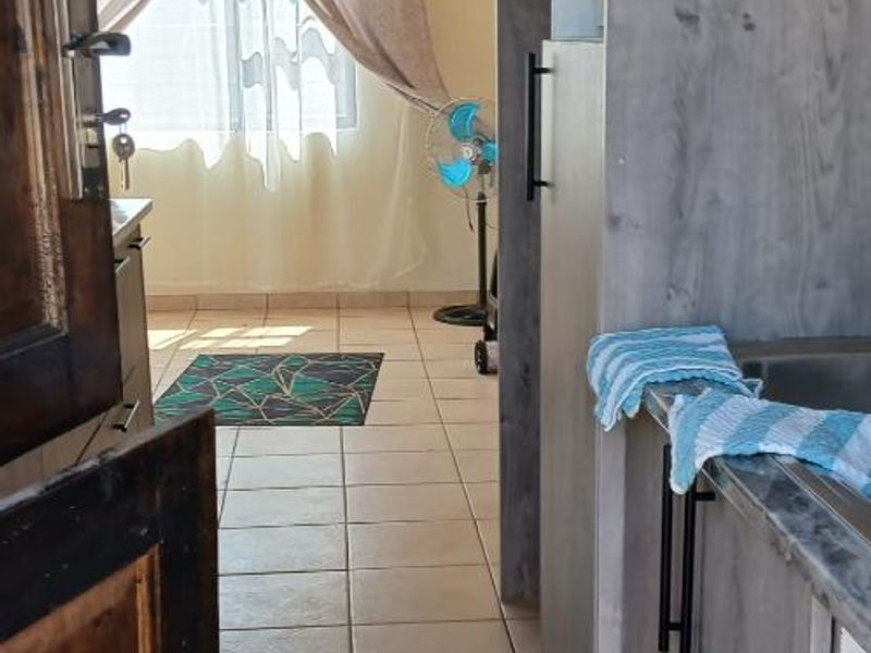 A functional kitchen area featuring built-in cabinetry, tiled flooring, and a sink, leading into an adjacent living space.