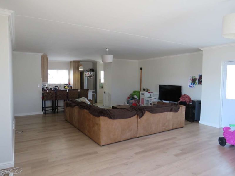Spacious open-plan living area featuring light laminate flooring, neutral walls, and a functional kitchen with island seating.