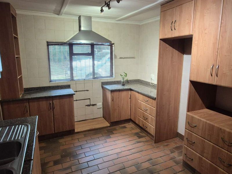 A functional kitchen featuring wood-look laminate cabinetry, granite countertops, a stainless steel extractor fan, and durable brick flooring.