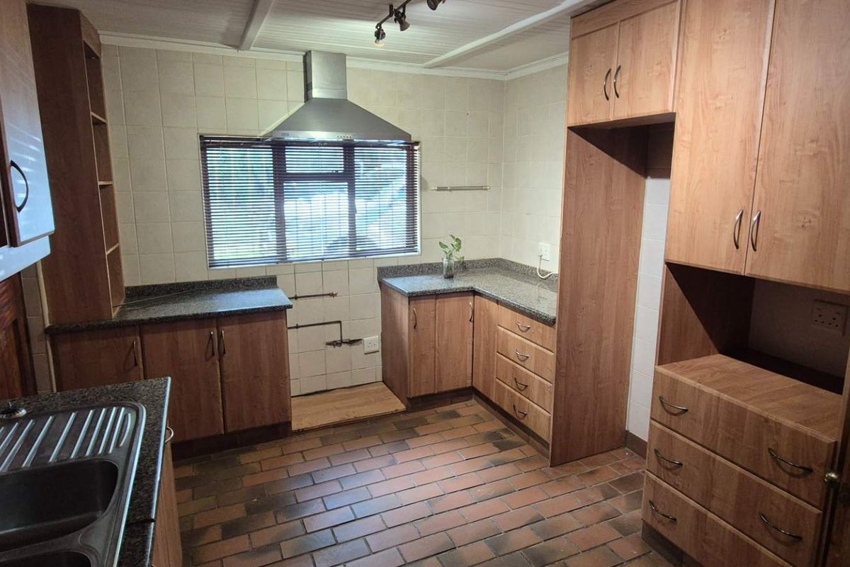A functional kitchen featuring wood-look laminate cabinetry, granite countertops, a stainless steel extractor fan, and durable brick flooring.