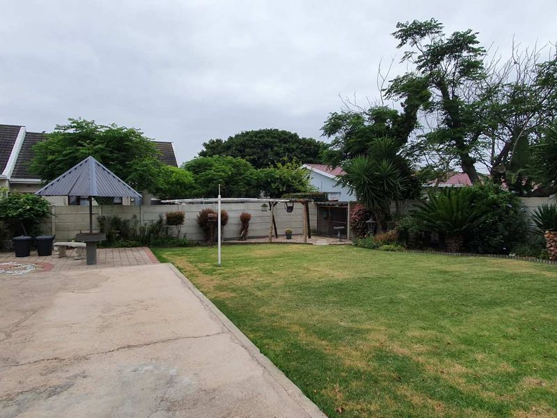 A spacious rear garden featuring a concrete patio, a fixed outdoor braai area, and a precast boundary wall, offering potential for landscaping improvements.
