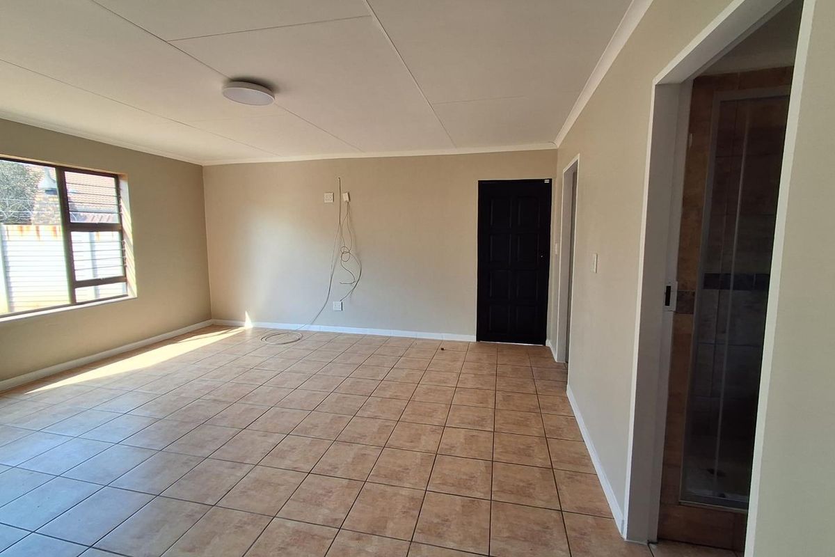 A spacious, empty living area featuring neutral wall tones, tiled flooring, and a large window, providing a blank canvas for interior design.