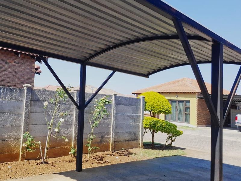 A functional metal carport structure providing covered parking, situated on a concrete driveway with a precast concrete boundary wall in the background.