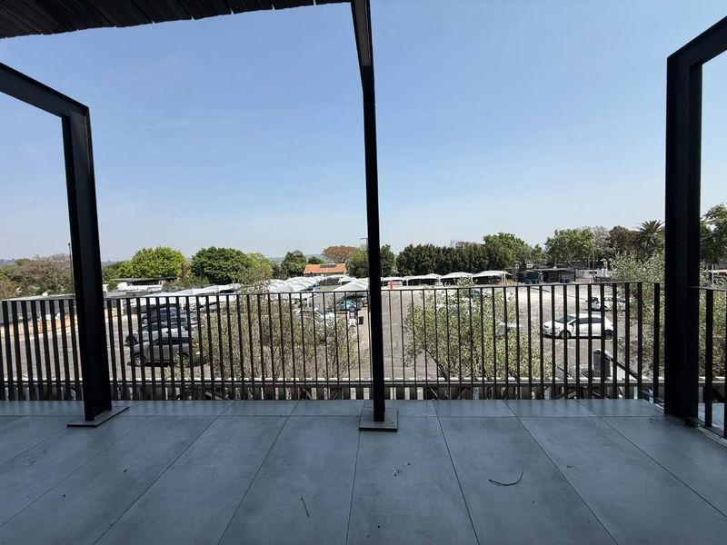 A modern covered balcony featuring tiled flooring and a sleek metal balustrade, offering an elevated view over the adjacent parking area.