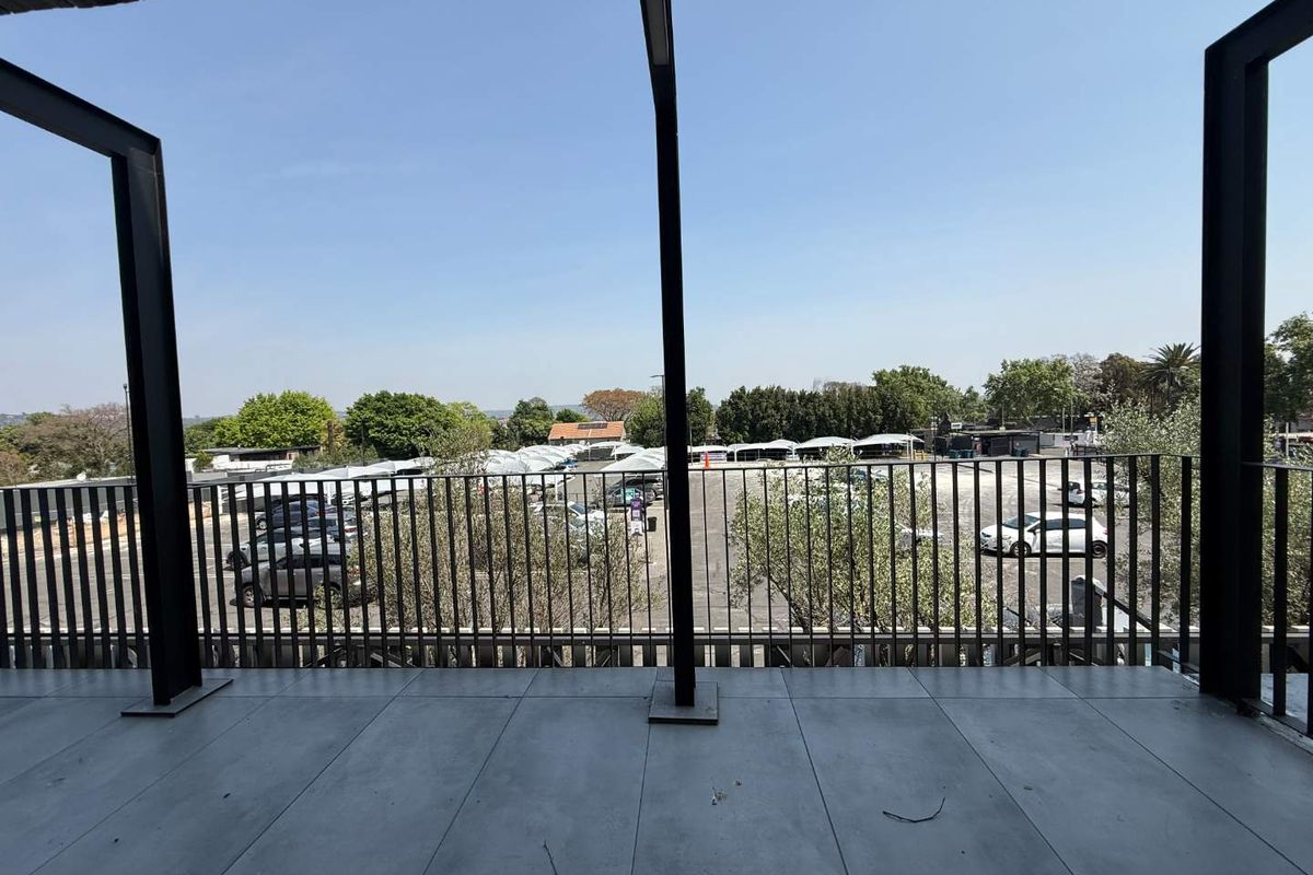 A modern covered balcony featuring tiled flooring and a sleek metal balustrade, offering an elevated view over the adjacent parking area.